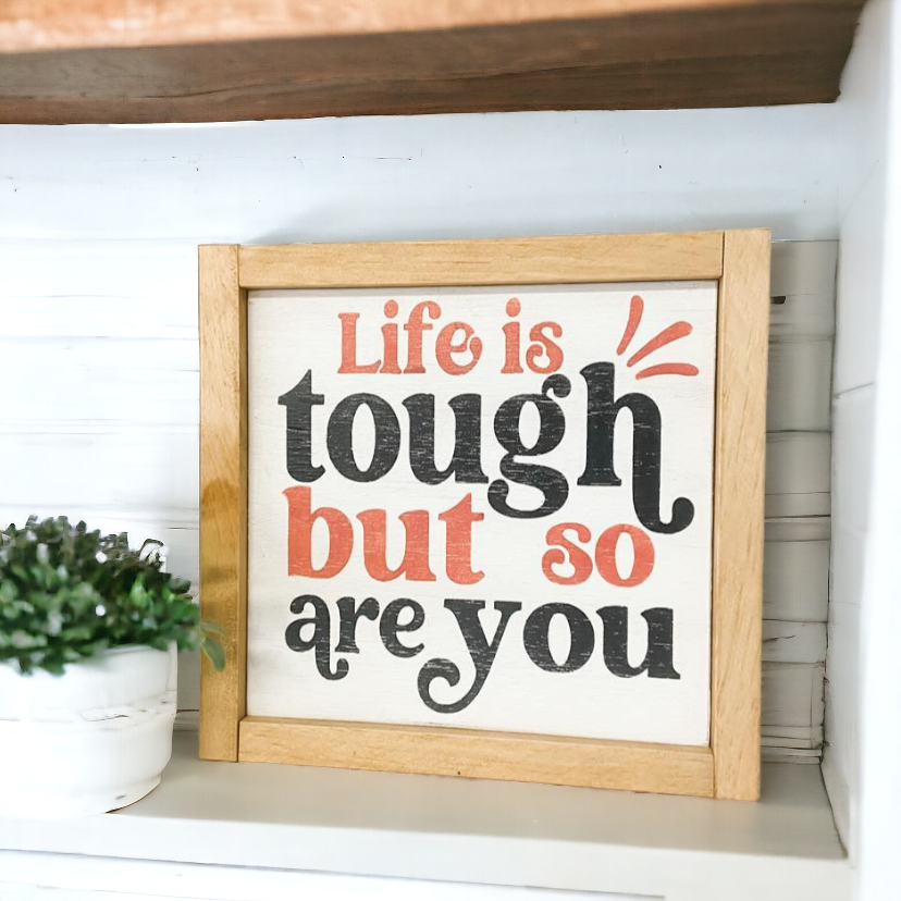 A 9.5" x 9.5" framed wood sign with a white background, featuring bold black and playful pink text that reads, 'Life is tough but so are you.' This versatile piece serves as rustic wall art and inspiring pink decor, making it an ideal decorative home decor addition to any room, including your home office