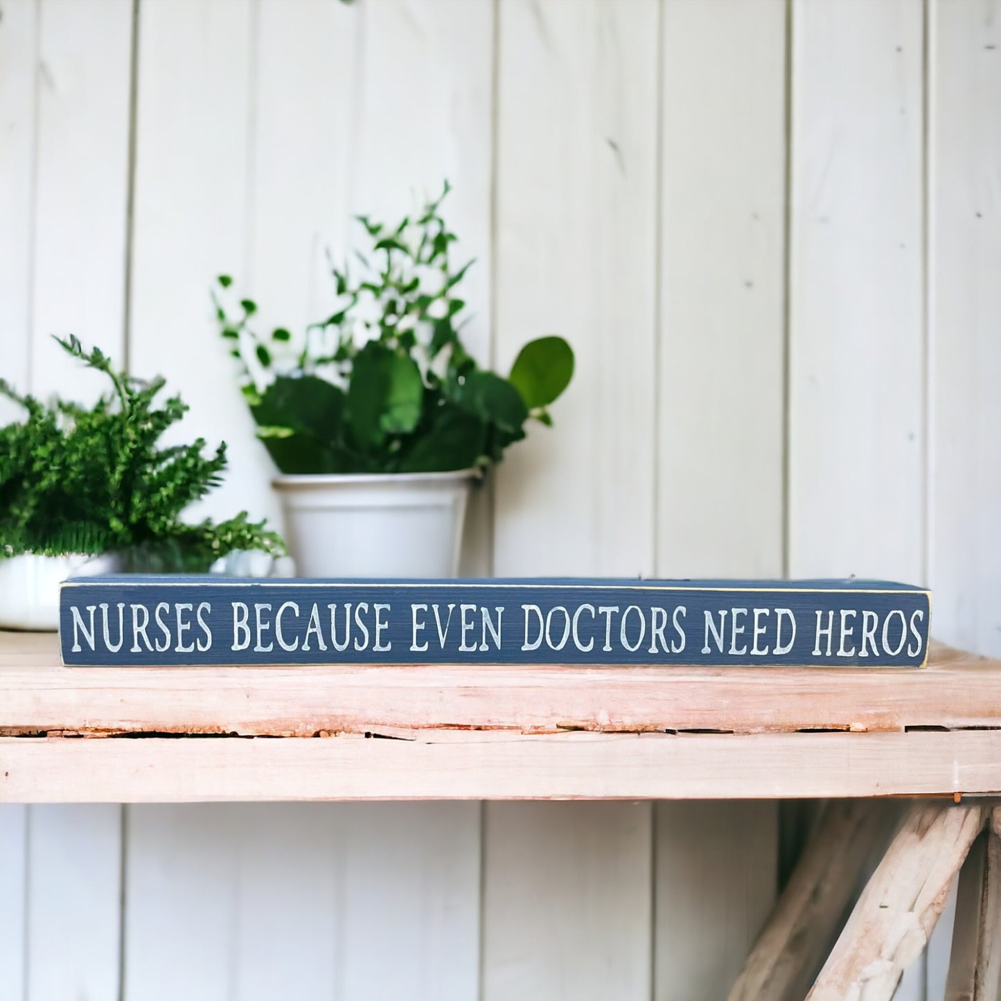 Handpainted bluish-gray wood sign with white text reading 'Nurses Because Even Doctors Need Heroes,' freestanding 16-inch gift decor for nurses.