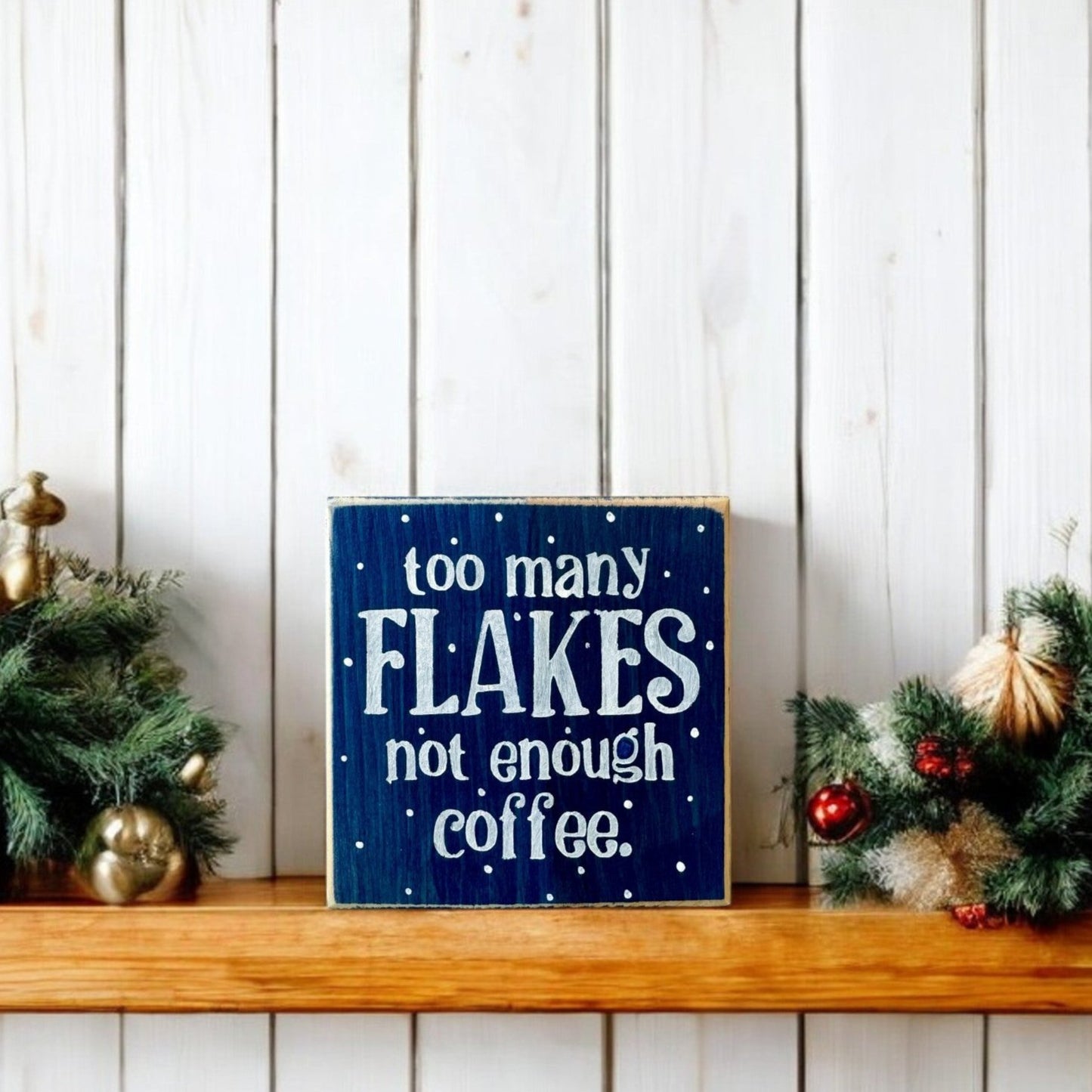 Handpainted wood block sign reading “Too Many Flakes, Not Enough Coffee” in white text on a navy blue background, surrounded by snowflakes, ideal for winter decor and coworker gifts.