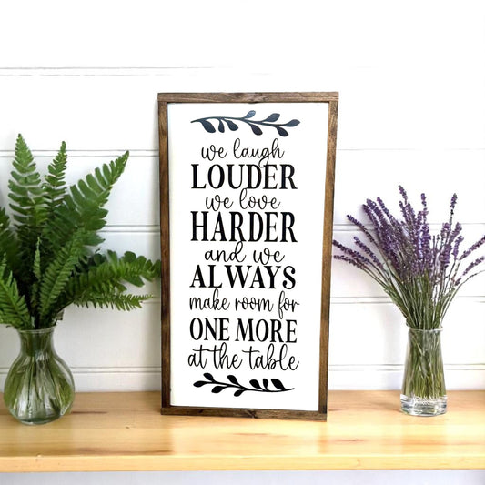 Framed farmhouse sign that reads "we laugh louder, we love harder, and we always make room for one more at the table"

