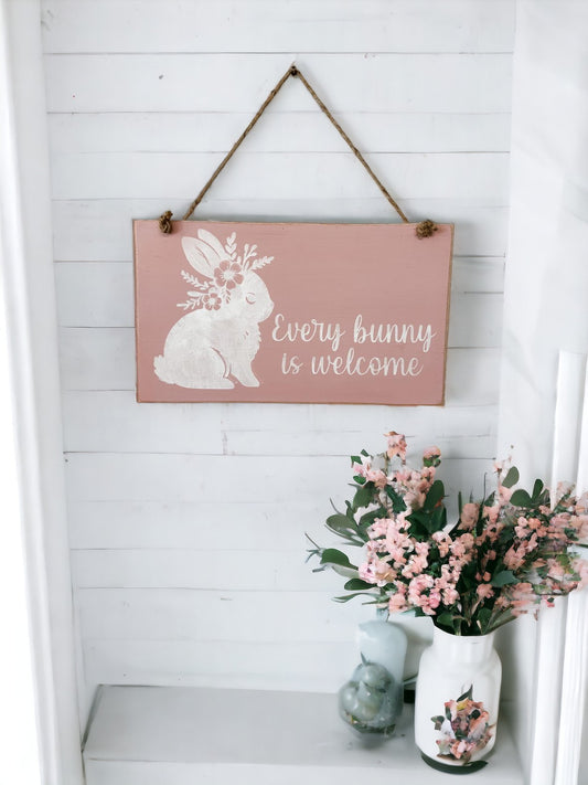 7" x 12" farmhouse hanging wood sign with 'Every Bunny Is Welcome' in white text on soft pink background