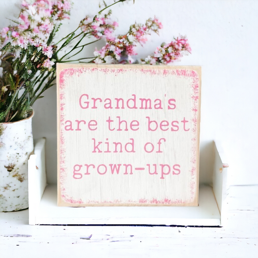 A 4.5" x 4.5" wood sign with a white background, playful pink text, and a vibrant pink border, featuring the message, 'Grandmas are the best kind of grown ups.' This charming grandma sign adds a playful and loving touch to your decor, making it an ideal gift or a delightful addition to your space