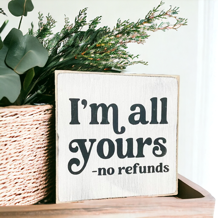 A 4.5" x 4.5" small wood sign with a white background and bold black text that reads, 'I'm all yours, no refunds.' This small wood sign is the perfect wood love sign, designed for couples who enjoy a touch of sarcasm and playful teasing, making it an ideal choice for a unique and light-hearted gift.