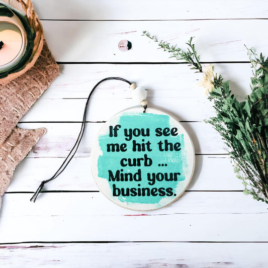 4-inch wooden car charm with teal brushstroke background, reading 'If you see me hit the curb, mind your business.