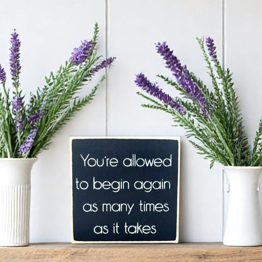 Mini wood block sign that reads “You're allowed to begin again as many times as it takes”