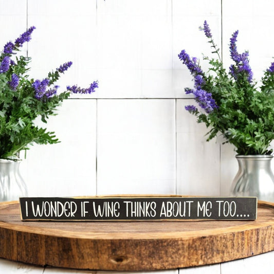 Black and white skinny wood sign with text reading 'I Wonder If Wine Thinks About Me Too...' - perfect funny wine saying and wine love gift.