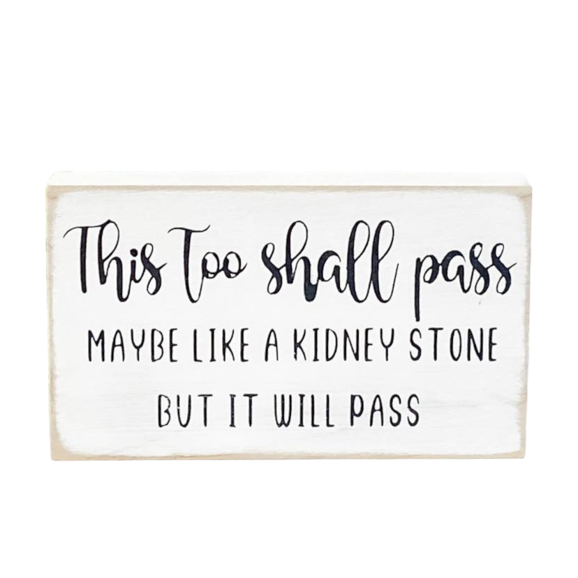 A 3.5" x 6" small wood sign with a white background and a humorous black text that reads, 'This too shall pass, maybe like a kidney stone but it will pass.' This freestanding sign is the perfect 'thinking of you' gift, offering humor and support as a funny adult gift for a friend who could use a good laugh during tough times.