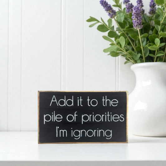 Handmade funny office desk sign reading “Add It to the Pile of Priorities I’m Ignoring” – sarcastic office decor, 3.5" x 6" wood block, witty workplace gift.