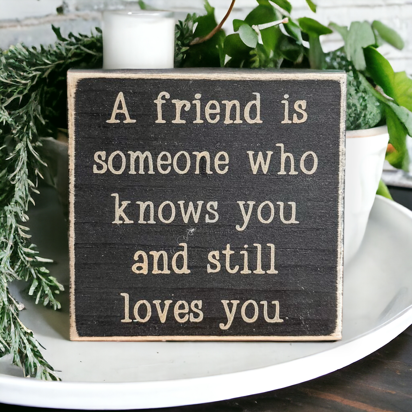 Image of a 4.5-inch wooden block sign with khaki text that reads, 'A friend is someone who knows you and still loves you.' Ideal decor and heartfelt gift for girls, emphasizing the essence of true friendship.
