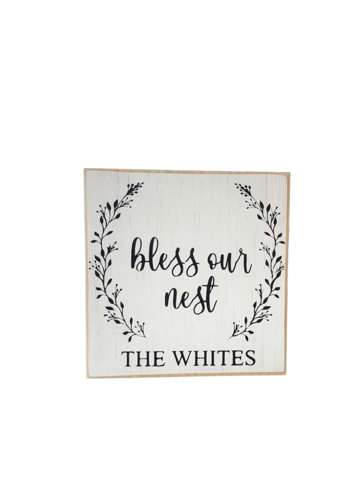  Personalized 5.5" x 5.5" wooden block sign with "Bless Our Nest" in black text, surrounded by a delicate spring floral wreath and a custom family name, hand-painted in a rustic modern farmhouse style.
