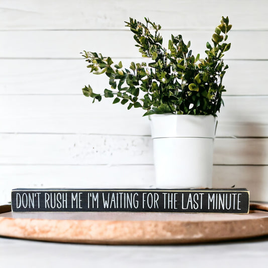 Handpainted black wood sign with white text reading 'Don't Rush Me I'm Waiting For The Last Minute,' freestanding 16-inch funny wood sign with a procrastination quote for office decor.