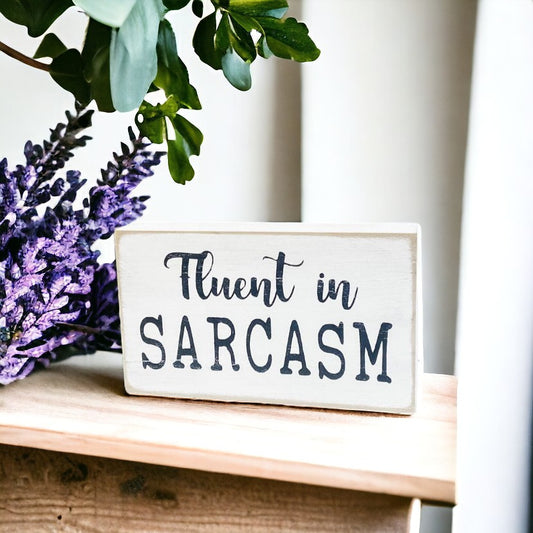 Fluent in Sarcasm" wooden block sign, hand-painted with black text on a white background, perfect for adding humor and personality to your home or office decor.