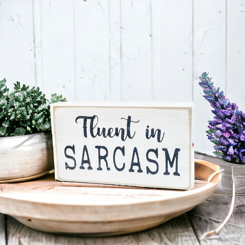 Fluent in Sarcasm" wooden block sign, hand-painted with black text on a white background, perfect for adding humor and personality to your home or office decor.