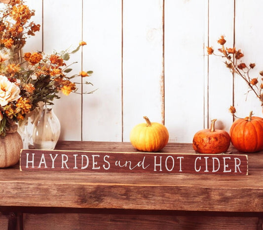 Rustic wood sign with white text reading 'Hayrides And Hot Cider' - perfect for autumn quotes and fall decorations.