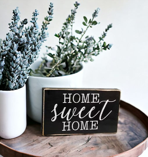 Home Sweet Home" hand-painted wooden sign with white text on a black background, displayed on a shelf.