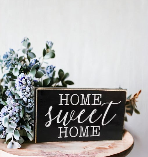 Home Sweet Home" hand-painted wooden sign with white text on a black background, displayed on a shelf.