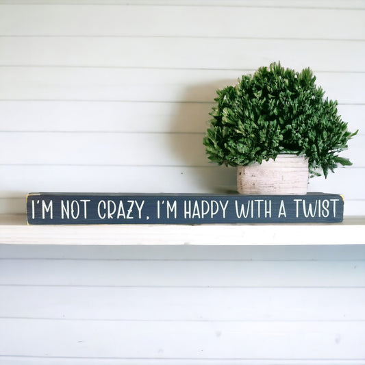 Handpainted bluish-gray wood sign with white text reading 'I'm Not Crazy, I'm Happy with a Twist,' freestanding 16-inch fun office decor for desks.