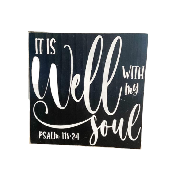 A 7" x 7" wood block sign with a black background and beautiful white text that reads, 'It is well with my soul.' This decorative wooden sign serves as a captivating piece of scripture art, inspired by Psalm 118:24, adding spiritual depth and beauty to your spac