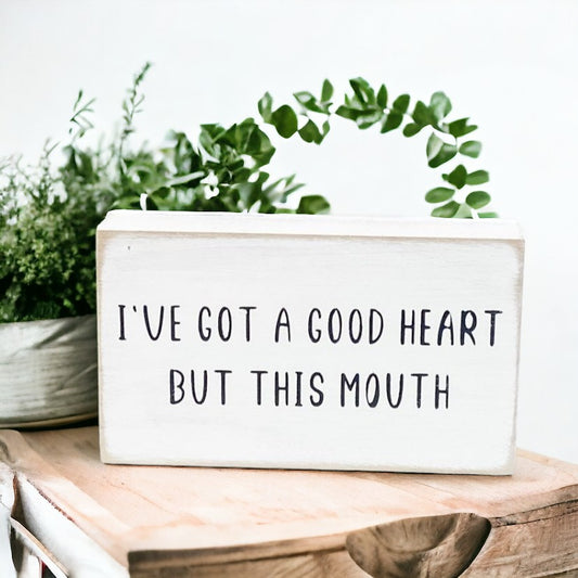 A 3.5" x 6" funny wood sign with a crisp white background and bold black text that reads, 'I've got a good heart but this mouth.' This freestanding sign is the perfect humorous gift, adding a touch of humor and sarcasm to your home or office decor as a funny office sign.