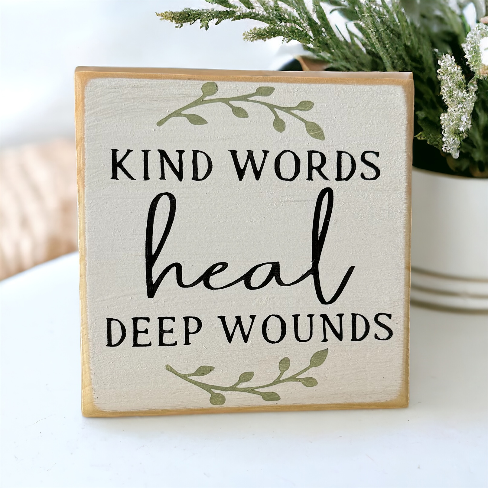 4.5" x 4.5" inspirational wood block sign with rustic black farmhouse text 'Kind words heal deep wounds' on a serene white background adorned with sage green botanical vines.