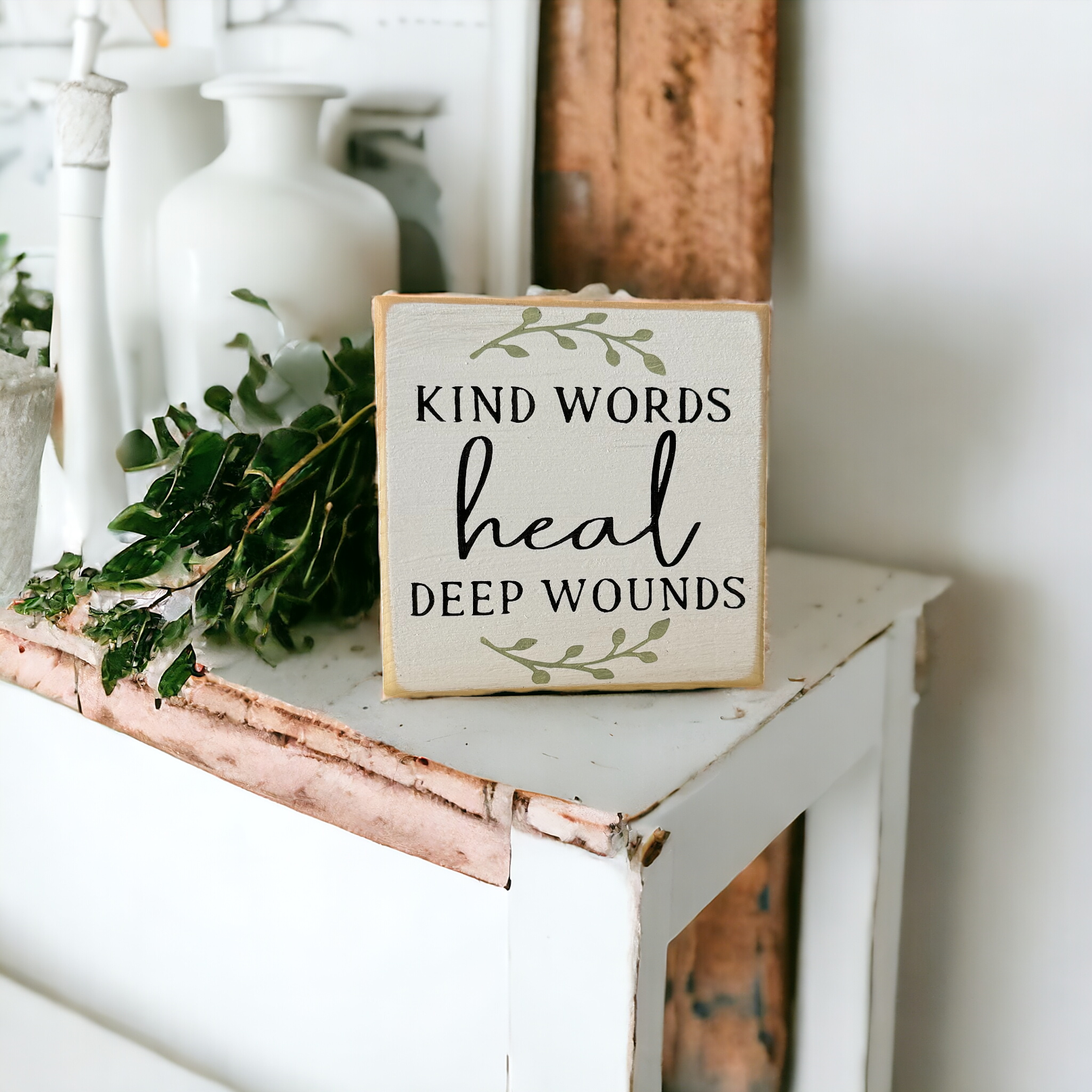 4.5" x 4.5" inspirational wood block sign with rustic black farmhouse text 'Kind words heal deep wounds' on a serene white background adorned with sage green botanical vines.