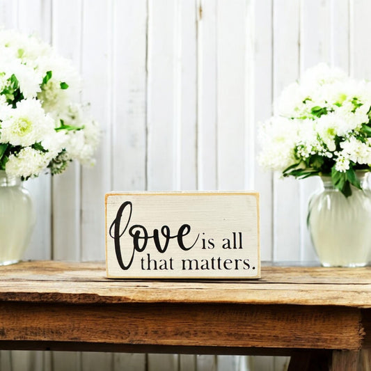 Hand-painted small wood sign reading 'Love is all that matters' in white with black text, perfect for Valentine's Day decor or as a romantic gift.