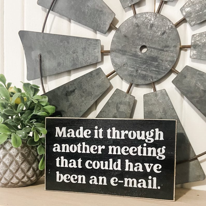 A witty mini wood sign, measuring 3.5" x 6", featuring the phrase, 'Made it through another meeting that could have been an email.' The sign is in bold white text on a black background. This funny decor piece is an ideal funny coworker gift or a hilarious gift for your boss, adding a touch of humor to your workspace.