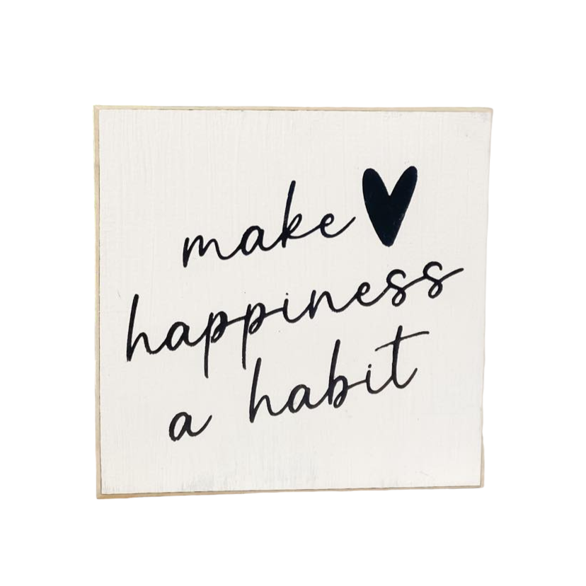 A 4.5" x 4.5" small wood sign with modern black text on a white background, displaying the inspirational happiness quote, 'Make Happiness A Habit.' This small wood sign is a charming addition to any space, serving as a reminder to prioritize joy and positivity