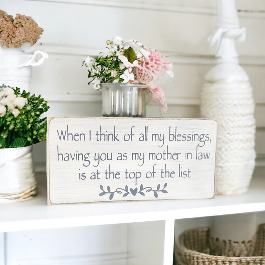 A 4" x 8" rustic wood sign with a white background and bluish gray text that reads, 'When I count all of my blessings, having you as my mother in law is at the top of my list.' This versatile rustic wood sign, perfect for a mother-in-law Christmas gift, is both free-standing and equipped with hanging hardware for easy wall display.