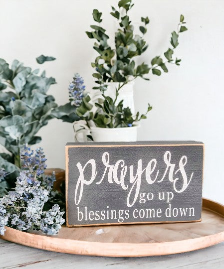 Prayers Go Up Blessings Come Down" wood sign with white text on gray background, displayed on a shelf