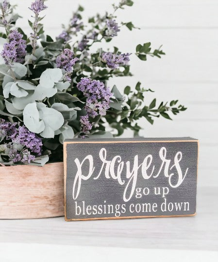 Prayers Go Up Blessings Come Down" wood sign with white text on gray background, displayed on a shelf