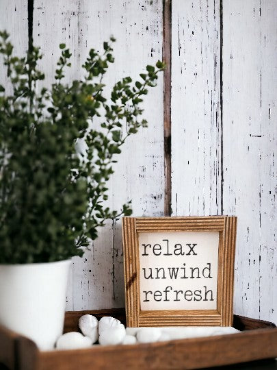 Hand-painted "Relax Unwind" bathroom sign with white background and black text, framed in dark stained wood, measures approximately 4" x 4".