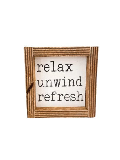 Hand-painted "Relax Unwind" bathroom sign with white background and black text, framed in dark stained wood, measures approximately 4" x 4".