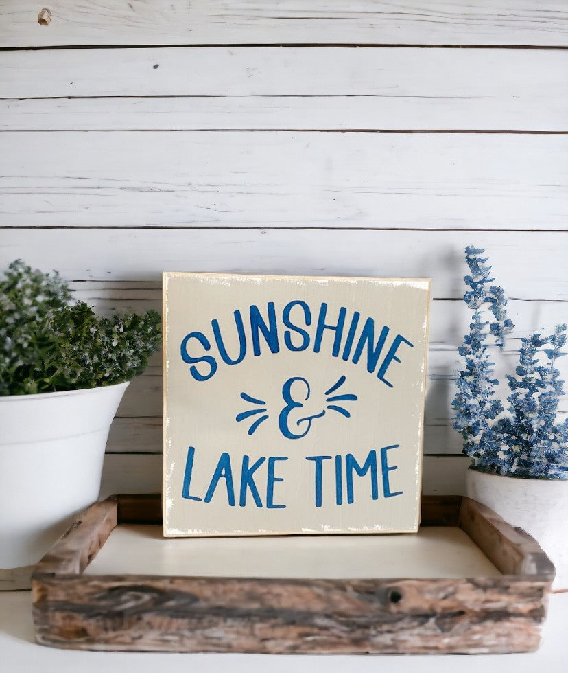 Image of a handcrafted grey wooden sign with navy blue text that reads 'Sunshine and Lake Time,' ideal for summer home decor.