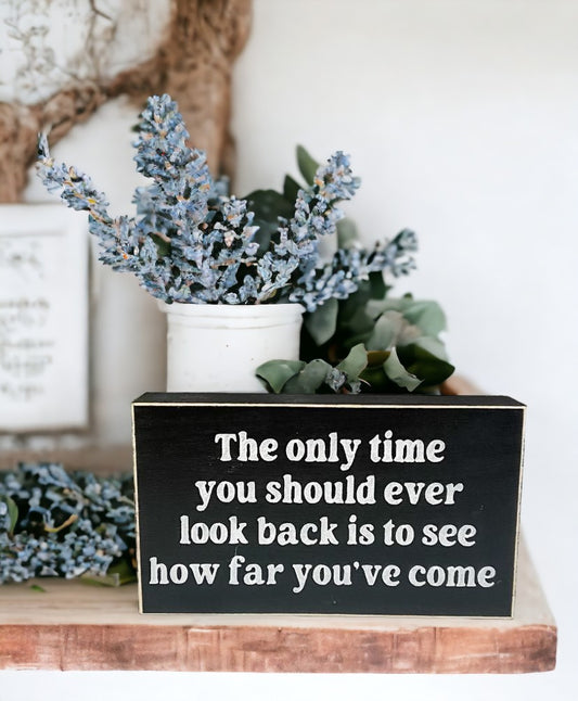 Inspirational wood sign with white text on black background, reading "The Only Time You Should Ever Look Back Is To See How Far You've Come", perfect for tabletop or shelf display.