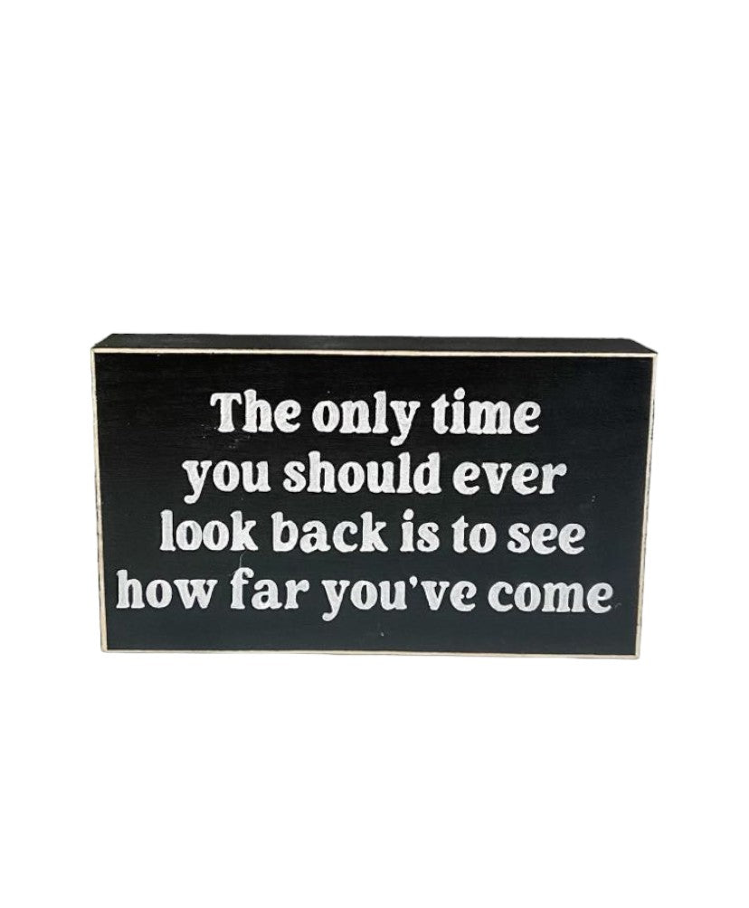 Inspirational wood sign with white text on black background, reading "The Only Time You Should Ever Look Back Is To See How Far You've Come", perfect for tabletop or shelf display.