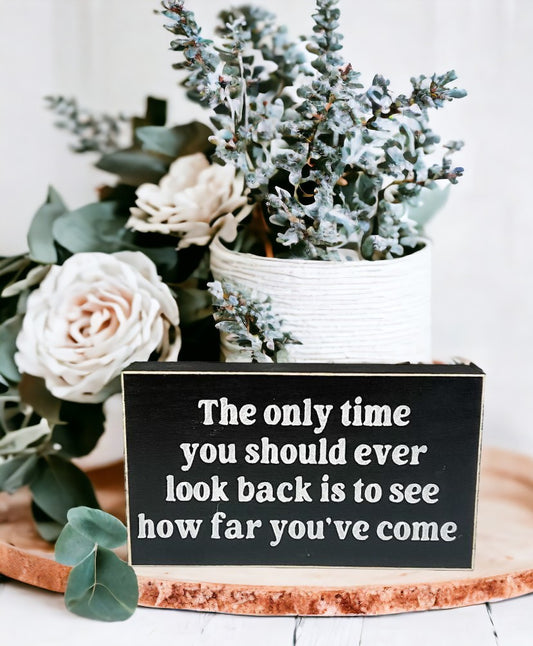 Inspirational wood sign with white text on black background, reading "The Only Time You Should Ever Look Back Is To See How Far You've Come", perfect for tabletop or shelf display.