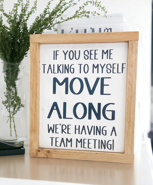 A framed wooden sign measuring 8" x 9.25". The sign features the humorous text, 'If you see me talking to myself, move along, we're having a team meeting.' This funny wood sign makes a great coworker gift and adds a playful touch to any office space.