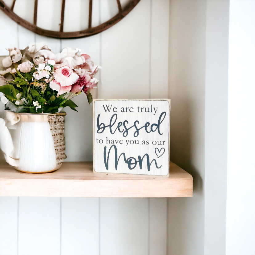 A 4.5" x 4.5" wood sign with a white background and elegant black text that reads, 'We are truly blessed to have you as our mom.' This unique mom gift is a heartwarming addition to your holiday decor, perfect for surprising your mom this Christmas.