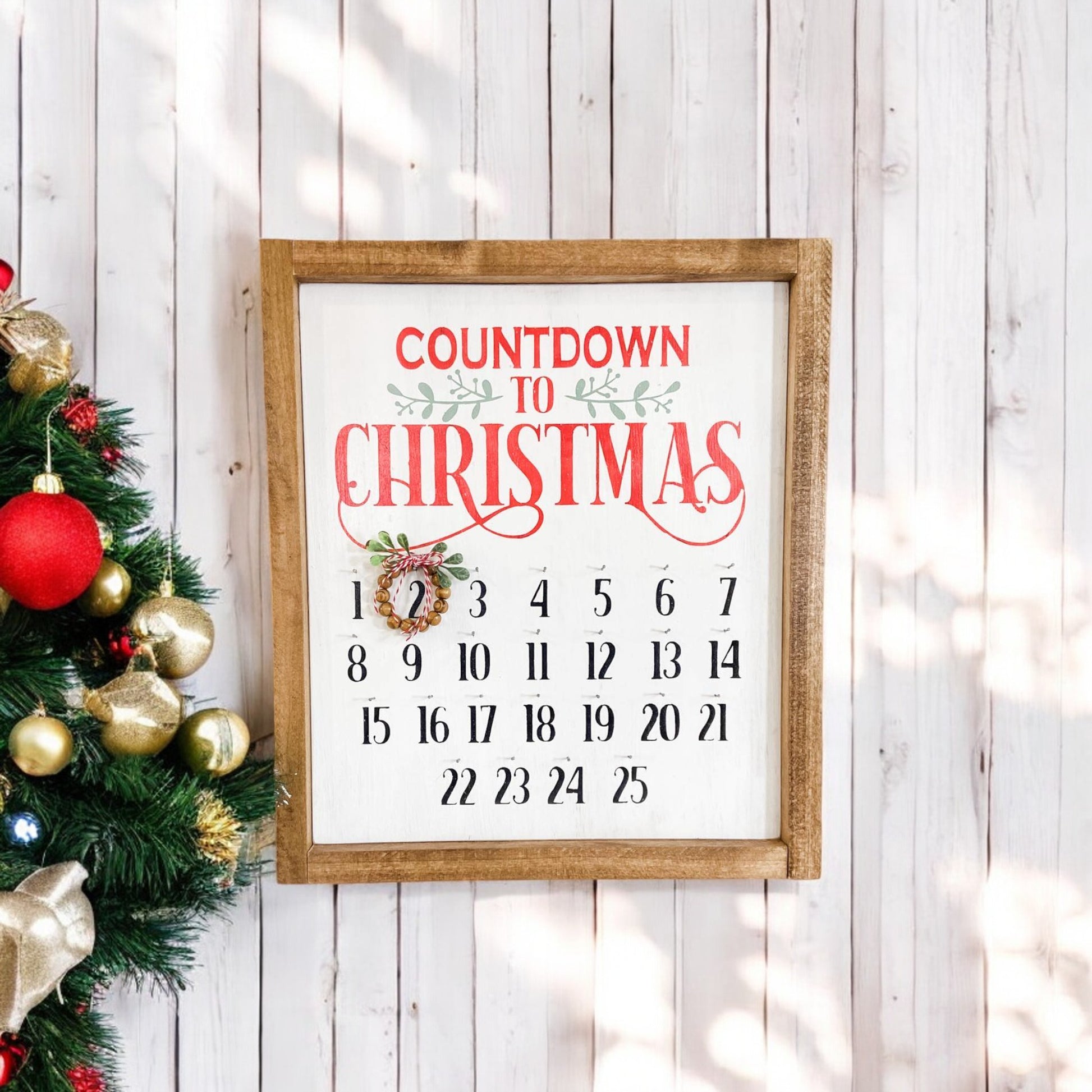 Framed wooden Christmas countdown sign with a movable bead wreath, handpainted white with red, green, and black text, perfect for hanging or displaying on a shelf.