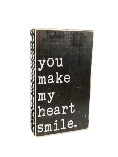 Hand-painted wood sign with white text on black background, featuring the phrase 'You Make My Heart Smile' surrounded by geometric design